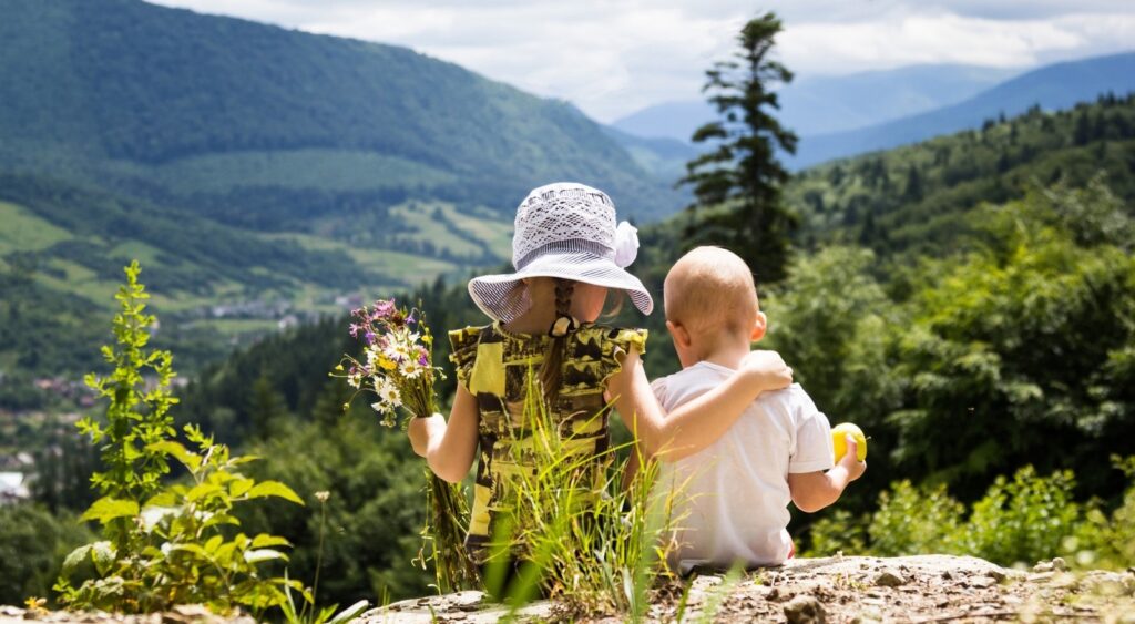 "Zwei Kinder sitzen umarmt in einer malerischen Berglandschaft."