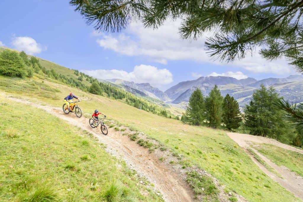 Zwei Mountainbiker fahren auf einem Pfad durch eine bergige Landschaft.