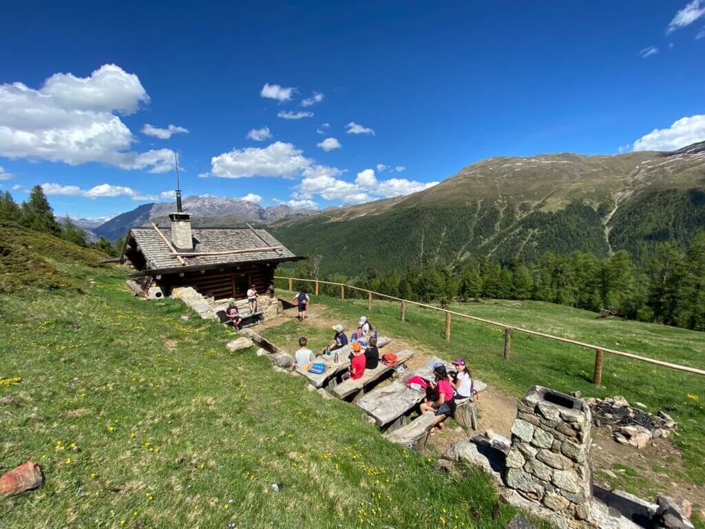 Eine Berghütte mit Menschen, die die Aussicht auf die umliegenden Berge genießen.